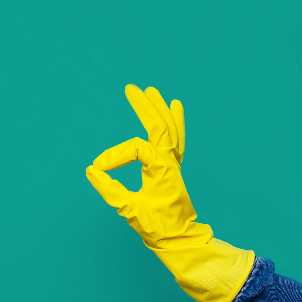 gele schoonmaak handschoen, duim en wijsvinger opelkaar in een rondje, uitdrukking oke. groene achtergrond